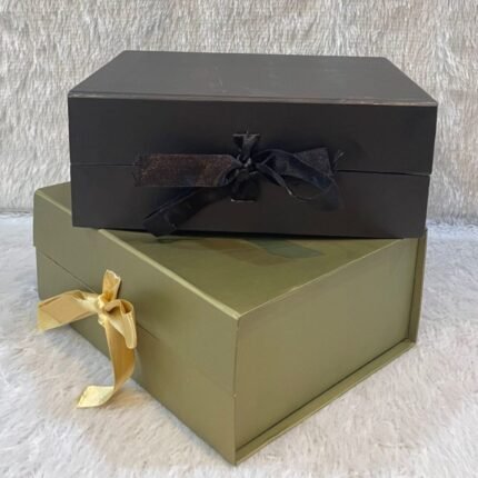 Corporate gift hamper boxes: black with matching ribbon, olive green with gold satin ribbon on white surface.