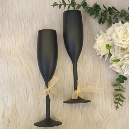 Matte black unbreakable champagne flutes with ribbon bows, ideal for corporate gifting, on elegant faux fur.